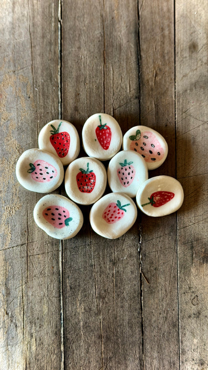 Close-up of a hand-painted ceramic strawberry worry stone with thumb groove.