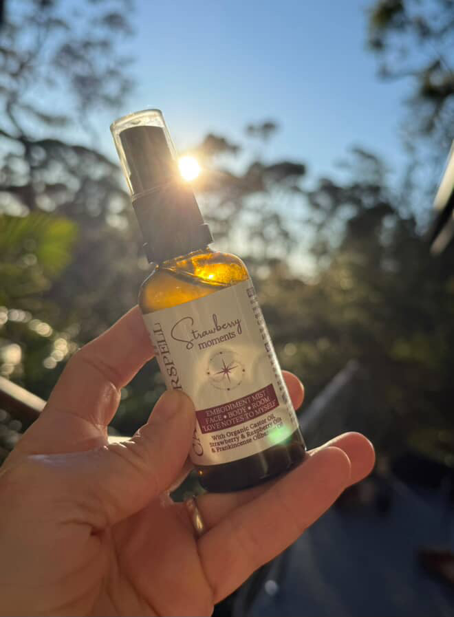 Hand holding a bottle of strawberry moments mist with a blurred natural background